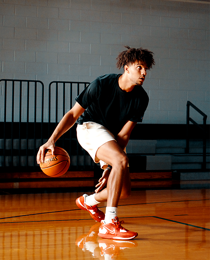 Male Model dribbling Legacy TF-1000 in cream colored shorts, black shirt and red shoes. 